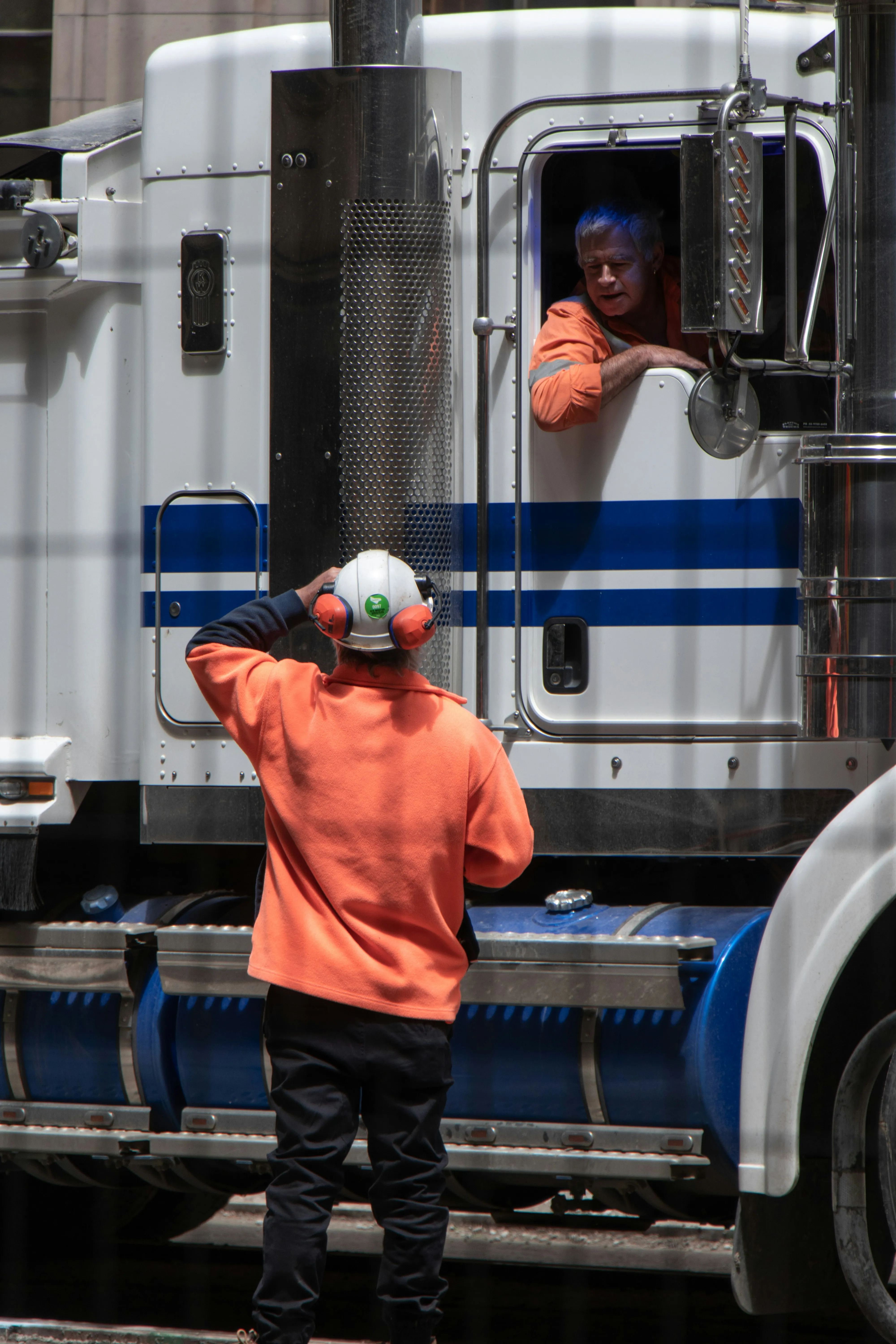 Truck driver speaking with a service technician beside a semi-truck